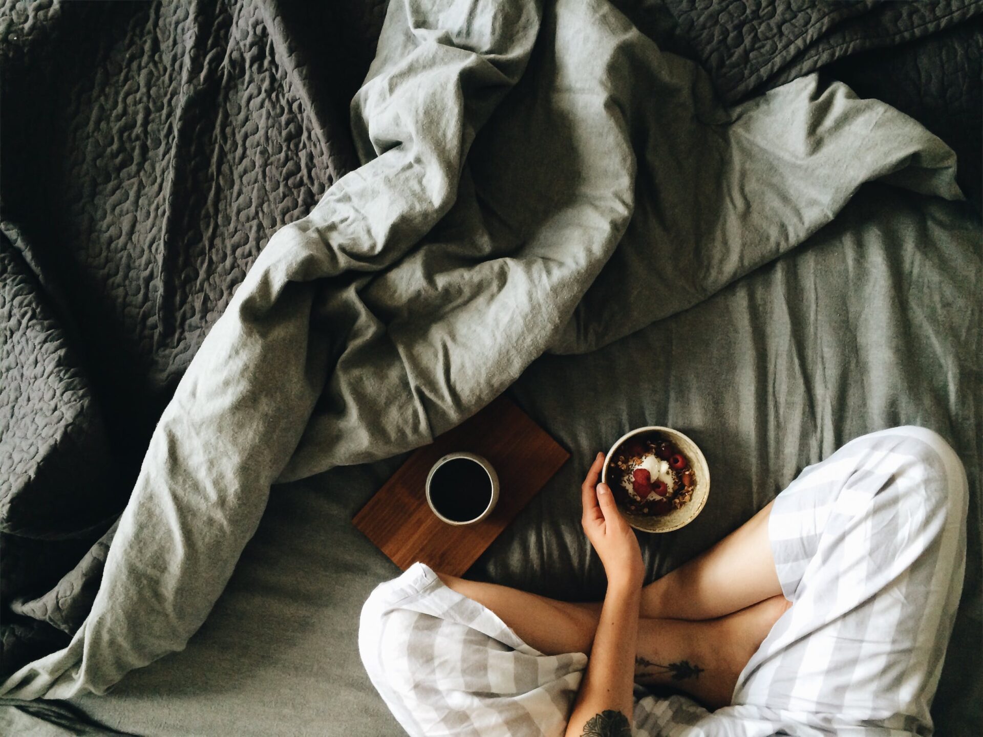 ベッドの上でコーヒーとヨーグルトを食べる人物の写真